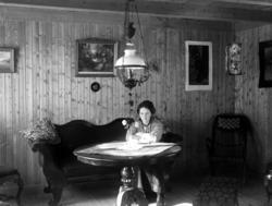 Kvinne sittende i et oppholdsrom med panelte vegger. Parafin