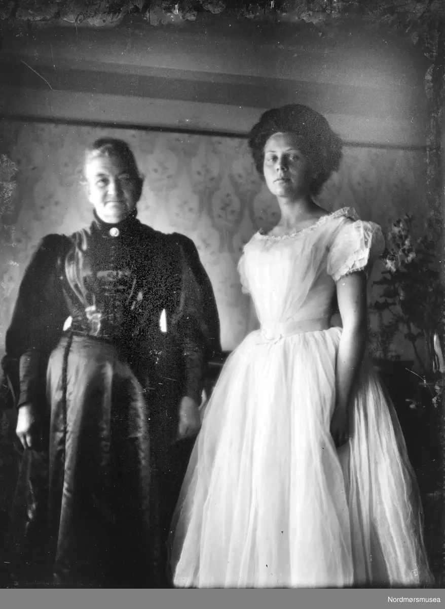 Foto av fru Gunhilde Helene Haagine Berner Sverdrup. (d. 1930). Gift med Henrik Lind Sverdrup (foreldre til Georg Sverdrup). Kvinnen i hvit kjole er ukjent. Det kan være et av barna/barnebarna til Henrik og Gunhilde. Datering er trolig omkring 1910 til 1919. Bildet er trolig fra Eidsvåg i Nesset kommune. Se også reg. nr. KMb-1987-005.4091. Fra Nordmøre museums fotosamlinger. EFR2015