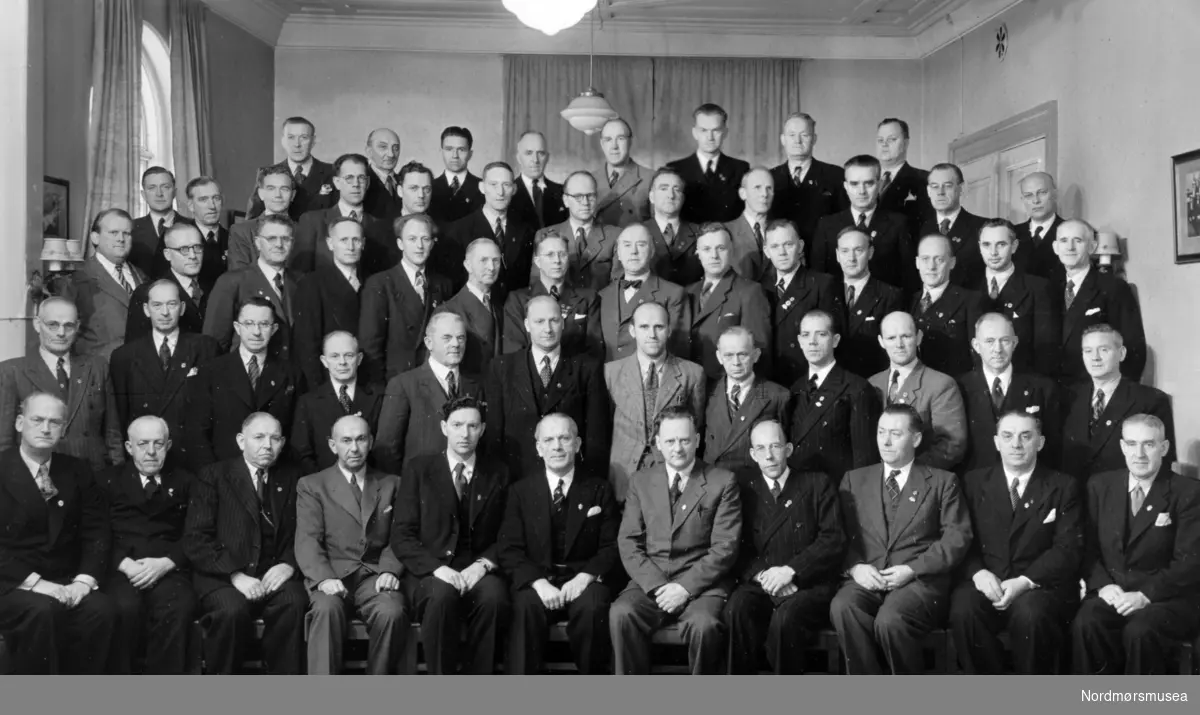 Norges landssangerforbunds representantskap. Trondheim 6. - 7. november 1948

1. rekke fra venstre: N. N. Krogeide, Oslo (revisor), Kristoffer Tønseth, Otta, M. Leikvoll, Bergen (varamann), Erling Gjerken, Bergen (styremedlem), Valter Aamodt, Bergen (sekretær), Karl Hjelmeland, Bergen (president), Anth. J. Nygård, Rosendal (visepresident), R. Keyser-Olsen, Haugesund (styremedlem), Andr. Lønnebotten, Bergen (styremedlem), Petro Johannessen, Bergen
(varamann) og
Hermod Rasmussen, Molde.

2. rekke fra venstre: Emil Olsen, Namsos, Thorstein Olsen, Oslo (revisor), Breder N. Haugstvedt, Bergen, Jens Lieblein, Drammen (Buskerud), Trygve Eng, Sarpsborg, Monrad Gulbrandsen, Notodden, Sigurd Berg, Raufoss, Otto Halln, Kr.sund N., R. Wang Olsen, Ålvik, Harald Holmedal, Bergen (Hordaland), Johs. Evertsen, Rjukan, Oscar Ottersen, Oslo.

3. rekke fra venstre: B. D. Øien, Trondheim, Otto Sørbye, Drammen, Anton
Bakhaug, Hamar, Annar Aaen, Tynset, Magne Løvik, Haugesund, S. Sahlin-Sveberg, Oslo, Arne Jareid, Drammen, Leif Balzersen, Oslo, Håkon Mentzoni, Sandnessjøen, Egill Helland, Bergen, Leif Eriksen, Bergen, Arnt Fuhre, Drammen, Finn Owren, Harstad og
Olaf Thomassen, Drammen (Buskerud).


4. rekke fra venstre: Kolbjørn Ødegård, Oslo (Akershus), Cato Gulbrandsen, Hamar, Paul Evensen, Oslo, Birger Hals,
Bodø, Arnt Holt, Sandvika, Hagerup Olsen, Sandnessjøen, Per Nilsen, Sandefjord, Asbjørn Pettersen, Gjøvik, Jens Nilsen, Hønefoss, Olaf Strugstad, Steinkjær, Frithjof Jacobsen, Sandvika og
Johs. Bækkelund, Oslo.


5. rekke fra venstre: Reidar Paulsen, Ålesund, Lars Aks, Kolbotn, Johan Andreassen, Laksevåg, John Moe, Levanger, Gustav Bengtzon, Narvik, Arne Eggan, Otta, Halvor Moe, Haugesund og
Karl Boquist, Narvik.

Fra Mannskoret ";Varde"; sine arkiver. Se også reg. nr. KMb-2009-009.0016x. Fra Nordmøre Museum sin fotosamling. Reg: EFR
