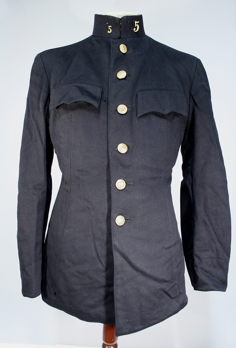 Mørkeblå uniformsjakke. Enkeltspent med seks knapper. To brystlommer, en innerlomme, stående krage med nr 5 i metall. Nummerne er forskjellig i størrelse.