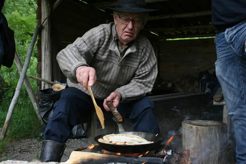 Mann sitter og steker fleskmonk i en gapahuk. Fleskmonk er tradisjonskost for skogsarbeidere.