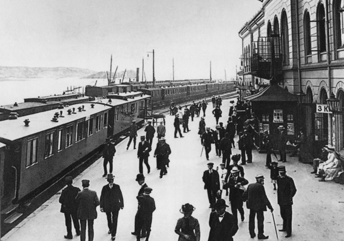 Drammen jernbanestasjon med flere tog og mange reisende på plattformen.