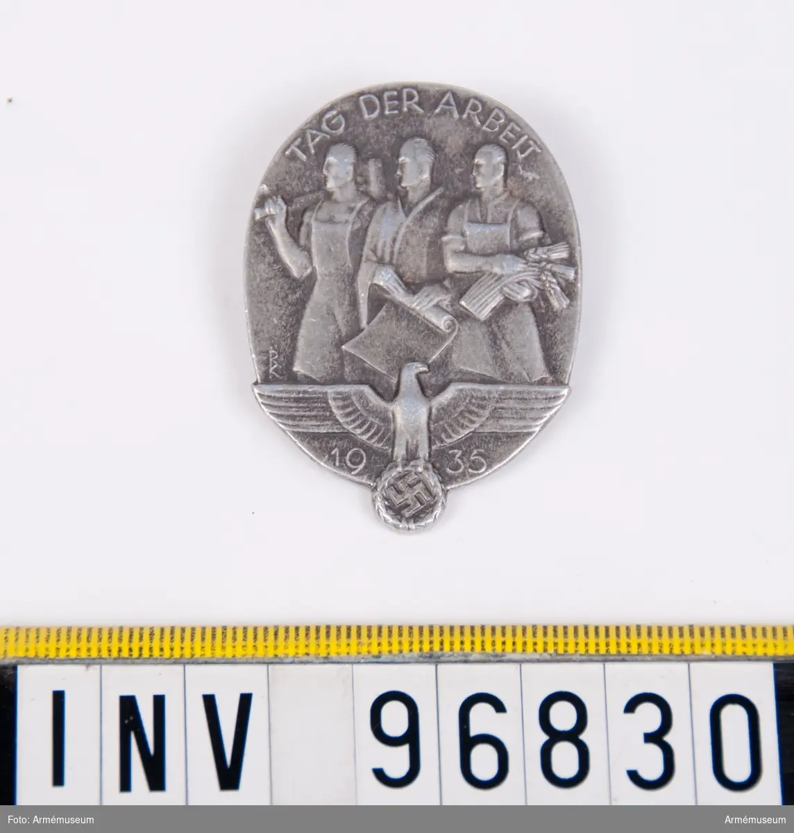 Propagandamärke i metall smyckat med motiv föreställande tre arbetare och den tyska örnen.