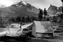 Folkevogn og telt foran ukjent fjellformasjon.