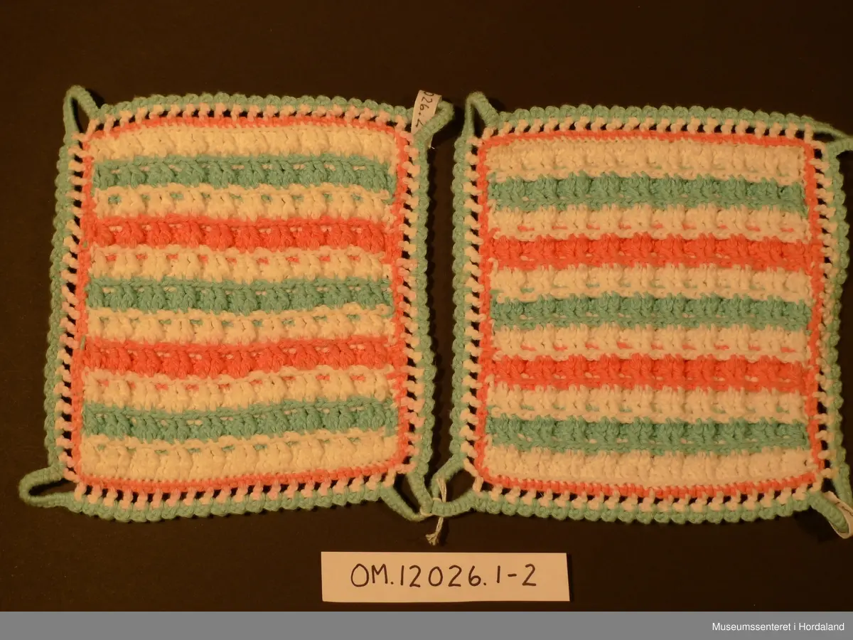 Firkanta grytelappar hekla i border med kvitt, rosa og lysgrønt garn. Rundt heile er det og ein heklakant i alle fargane, lysgrøn hempe i kvart hjørna.