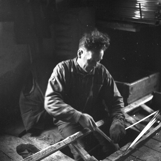 Reijmyre glasbruk 1957. Mannen "knäpper av" glasrör på dragbanan (det ligger en trave glasrör i bakgrunden).