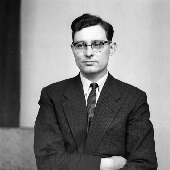 Foto av en okänd man i glasögon, klädd i mörk kostym och slips.
Midjebild, halvprofil. Ateljéfoto.