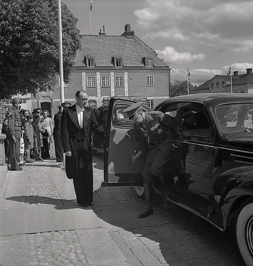 Kronprinsparet Gustaf Adolf och Louise anländer i bil till 
residenset. 
Kronprinsen är just på väg ut ur bilen, som öppnats av en
frackklädd betjänt. 
En del nyfikna har samlats i bakgrunden. 

Gustaf VI Adolf (1882-1973), reg. 1950-1973. (AB).