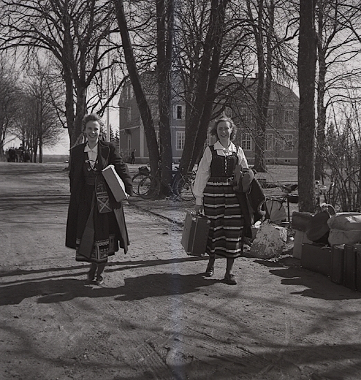 Avslutning vid Grimslövs folkhögskola.
Några unga kvinnor i folkdräkt (Värendsdräkt och till höger Rättviksdräkt) lämnar 
folkhögskolan, bärande på några väskor.