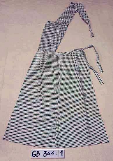 Midjeförkläde.
Kvalitet: bomullstyg med tryckt mönster.
Grönt och rosa mönster på vit botten. 
Modell: 3 våder i förklädeskjol, bröstlapp och breda hängslen samt 
knytband.
Inskrivet i huvudkatalogen 1996-1997.
Funktion: Skydd för kjolen.