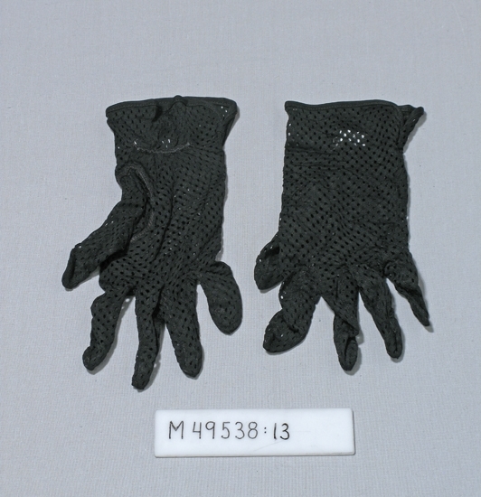 Svarta handskar/fingervantar av troligen syntetmaterial med genombrutet mönster, små ovala hål.
Kort resår (40 mm längd) på vantens krage, handledens insida.

Inskrivet i huvudbok 2008-05-07