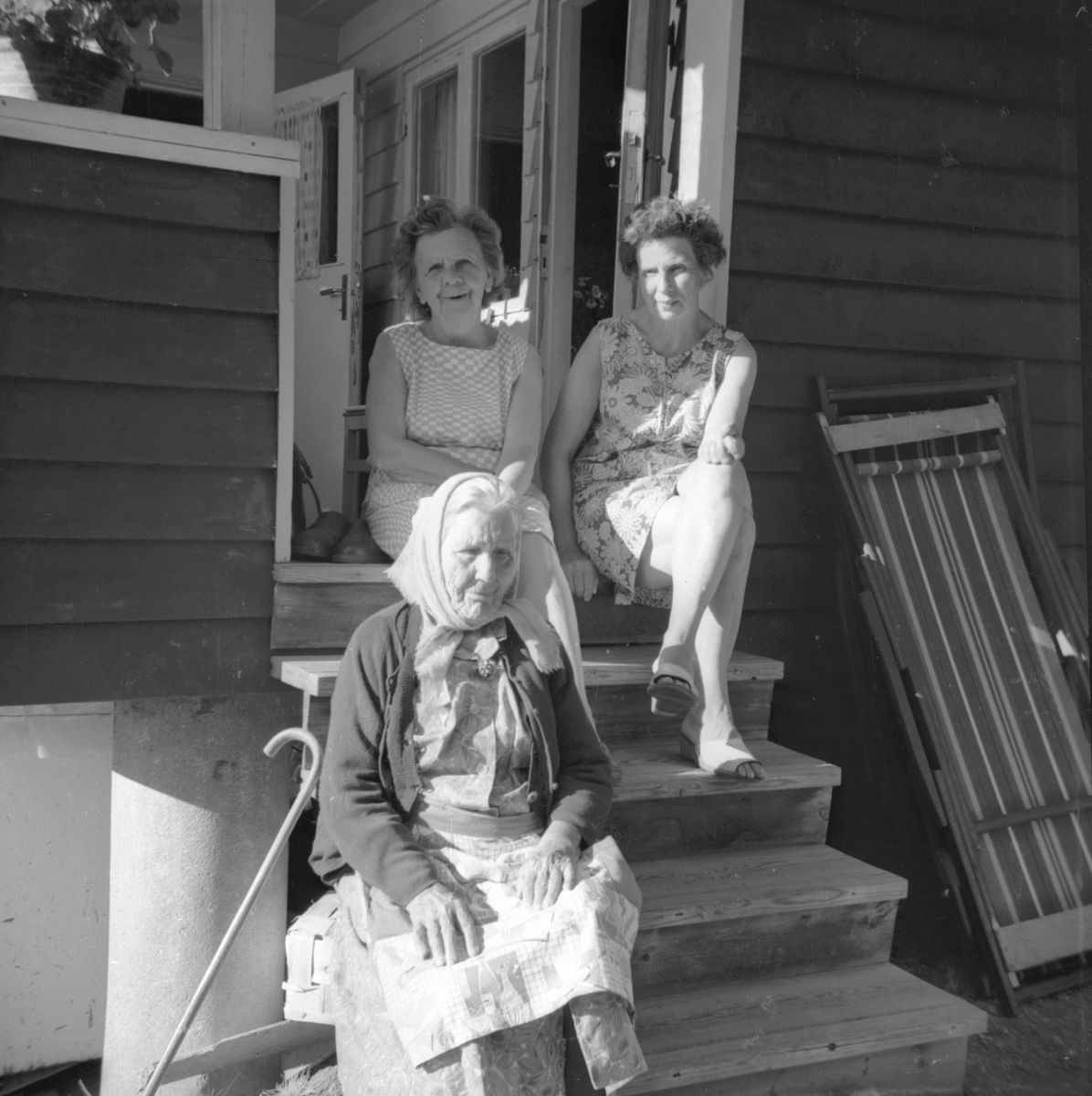 Tre kvinnor sitter på trappen till sommarstugan
