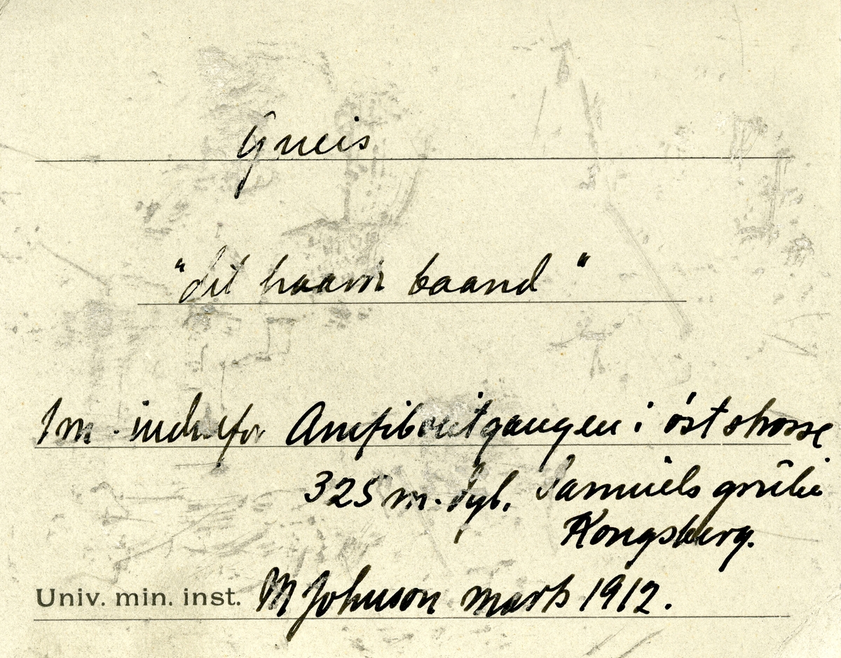 Etikett i eske:
Gneis
«det haarde baand»
1 m. indenfor Amfibolitgangen i øststrosse.
325 m. dyb. Samuels grube
Kongsberg.
M. Johnson marts 1912.

+ papirlapp