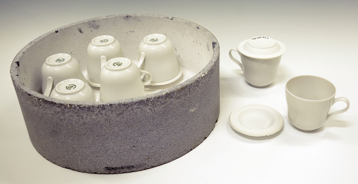 Rund kapsel i ildfast stein med syv porselenskopper på bumser/styringer (Merket A-G).