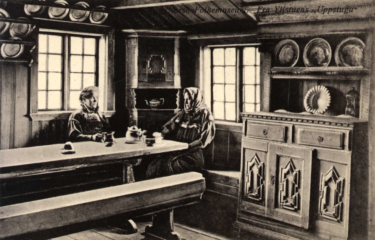Postkort. Ylistuens "Uppstugu", to kvinner ved langbordet. Telemarkstunet, NF.