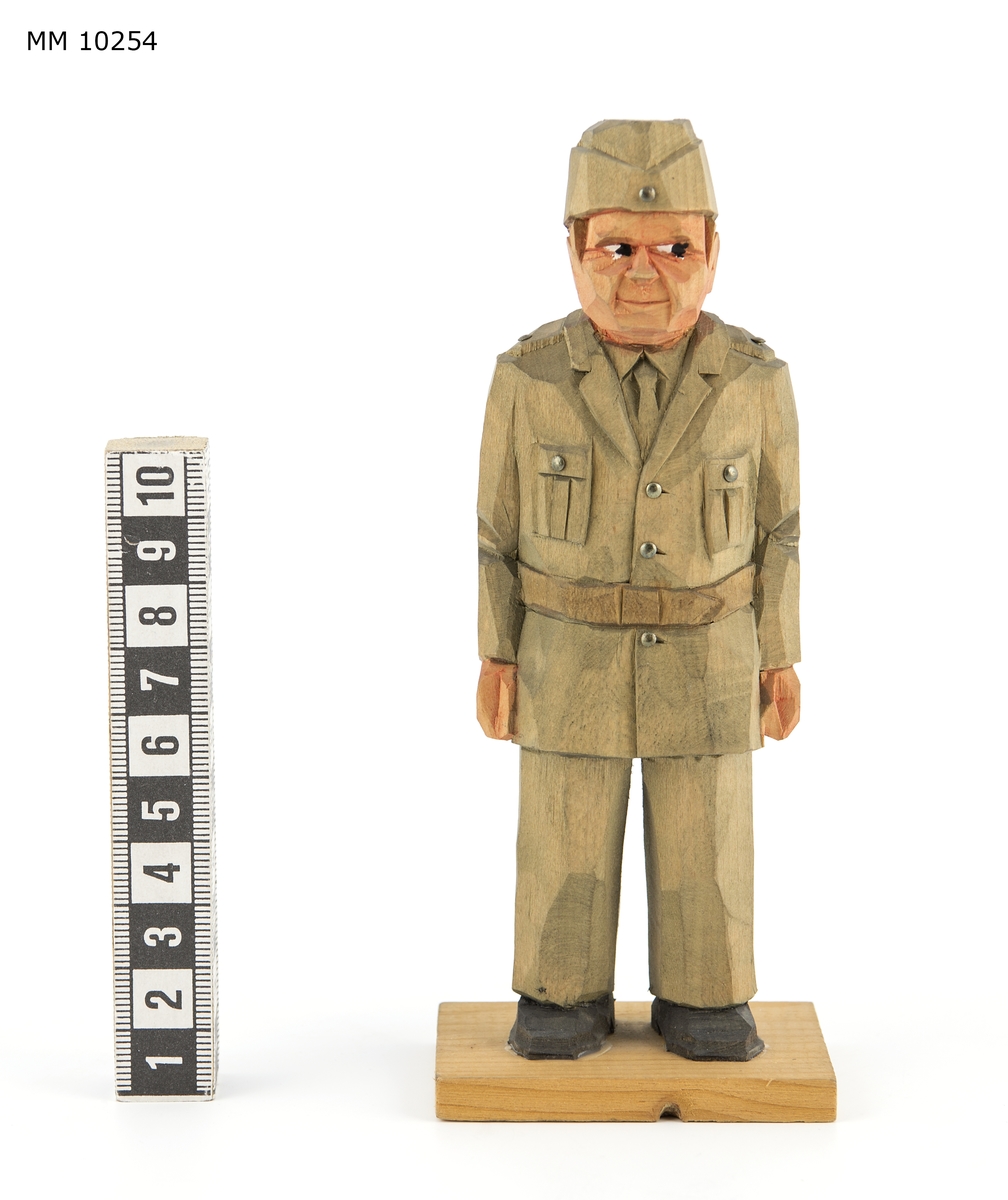 Skulptur. Föreställer en militär i uniform m/1942. Fastatt på en platta av trä.