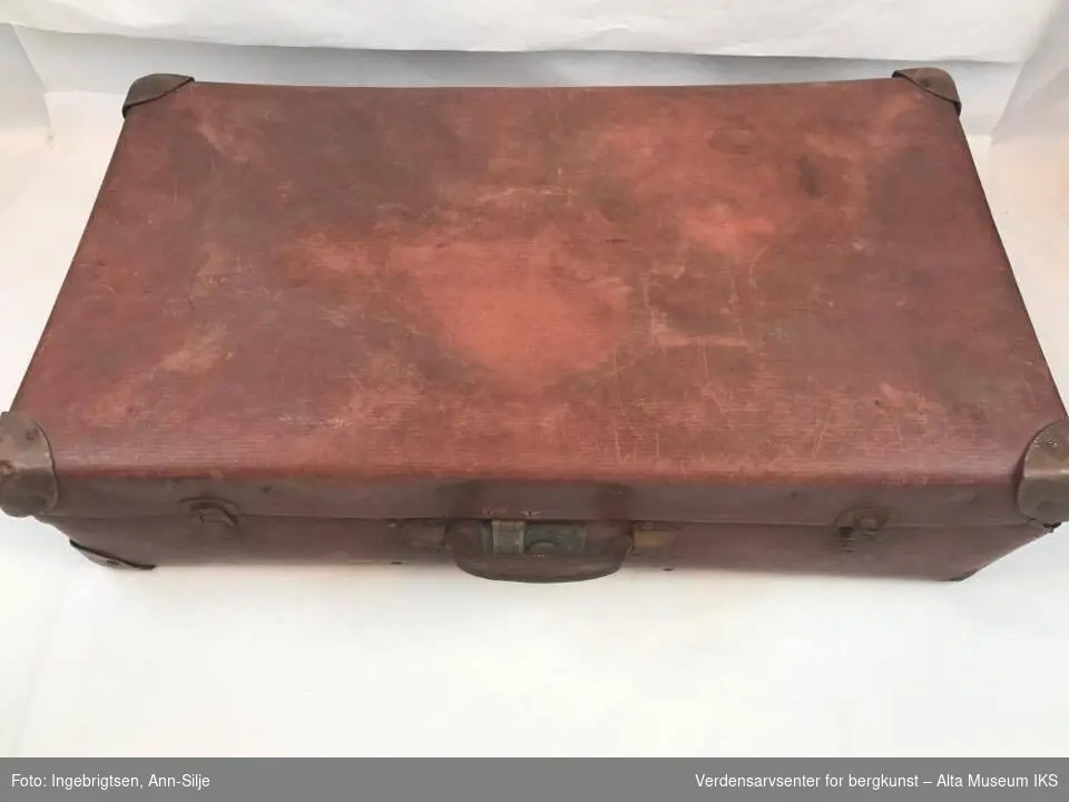 Rektangulær koffert med håndtak. Håndtaket er i metall, det samme er henglsene og låsen.