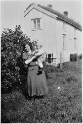 Kvinne og barn i hagen foran huset.