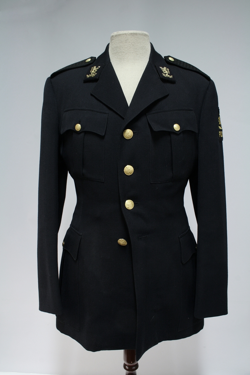 Enkeltkneppet jakke med fire riksløveknapper, fire ytterlommer, broderte riksløver på kragespeil, politimerke på ermet, og sorte skulderklaffer.