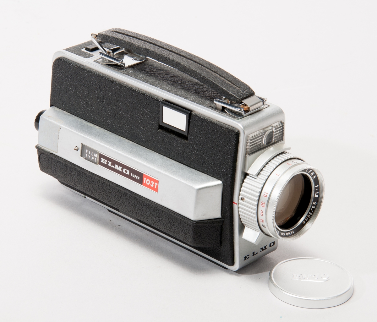 Filmkamera för smalfilm, Elmo typ Super 103T. 
Objektiv Elmo Zoom Lens 1:1,89,5/30 mm, med linslock. En spegel kan fällas ut för funktionen "Superimpose".
Tillverkningsnr. 327614.