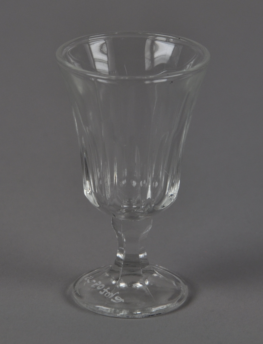 Drammeglass med fasetterte mønster på glass og stett. Glasset har utstående munnerand.