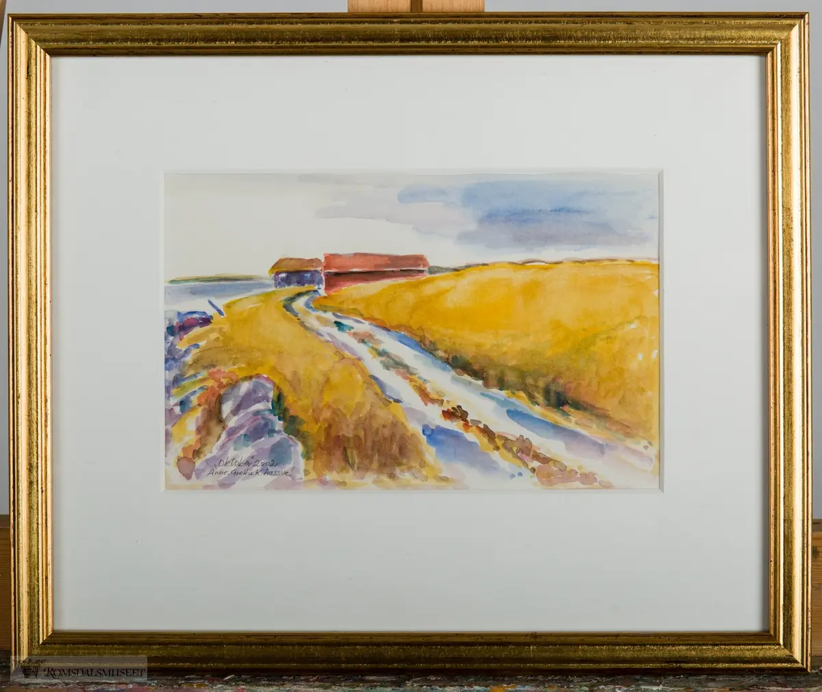 Et høstlandskap med kornåkre ned mot sjøen. En vei går gjennom åkeren og ender opp ved en låve og et hus/hytte.