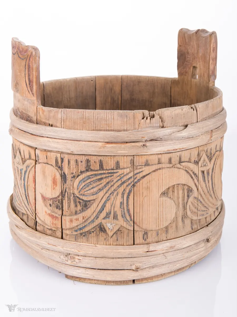 Rund med 3 vidjeband nede og 2 oppe og ører til lokk som mangler. Utskjæringer i relieff på hver stav.