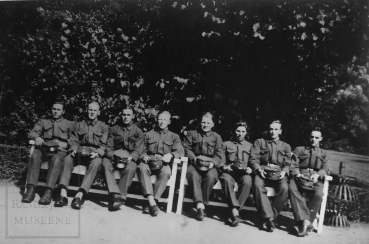 8 menn i uniform sitter ute på 2 benker.