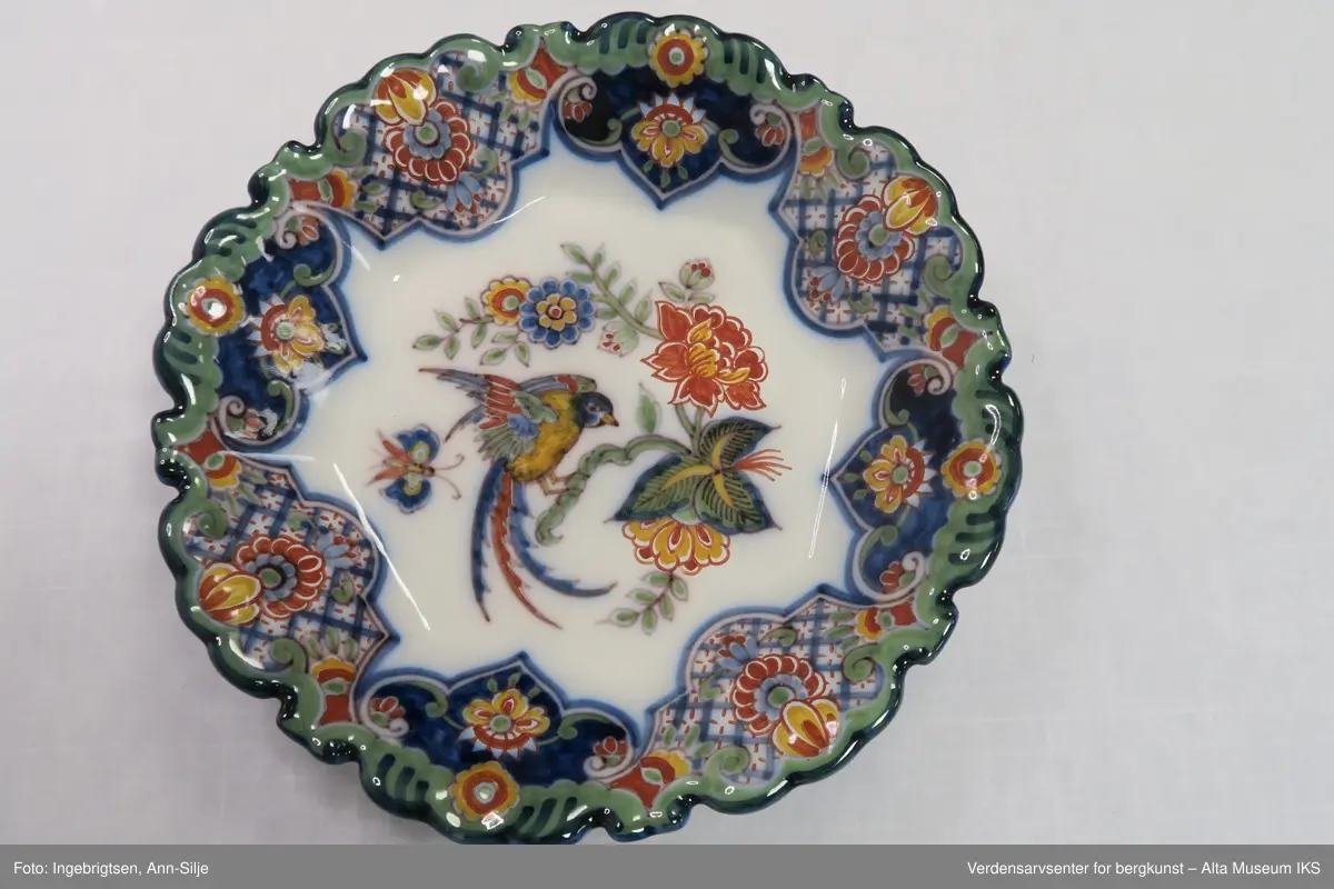 Fat, eller skål, med rund base, og svakt 8-kantet korpus og tunget kant. Motivet i fatet er ornamentalt blomster-, fugle- og sommerfuglmotiv. På baksiden er det motiver av spiraler og ruter.