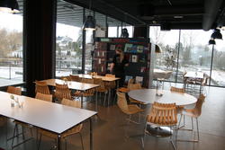 Interiørbilde fra Kafe Standpunkt viser stoler og bord, i bakgrunnen vindu fra gulv til tak