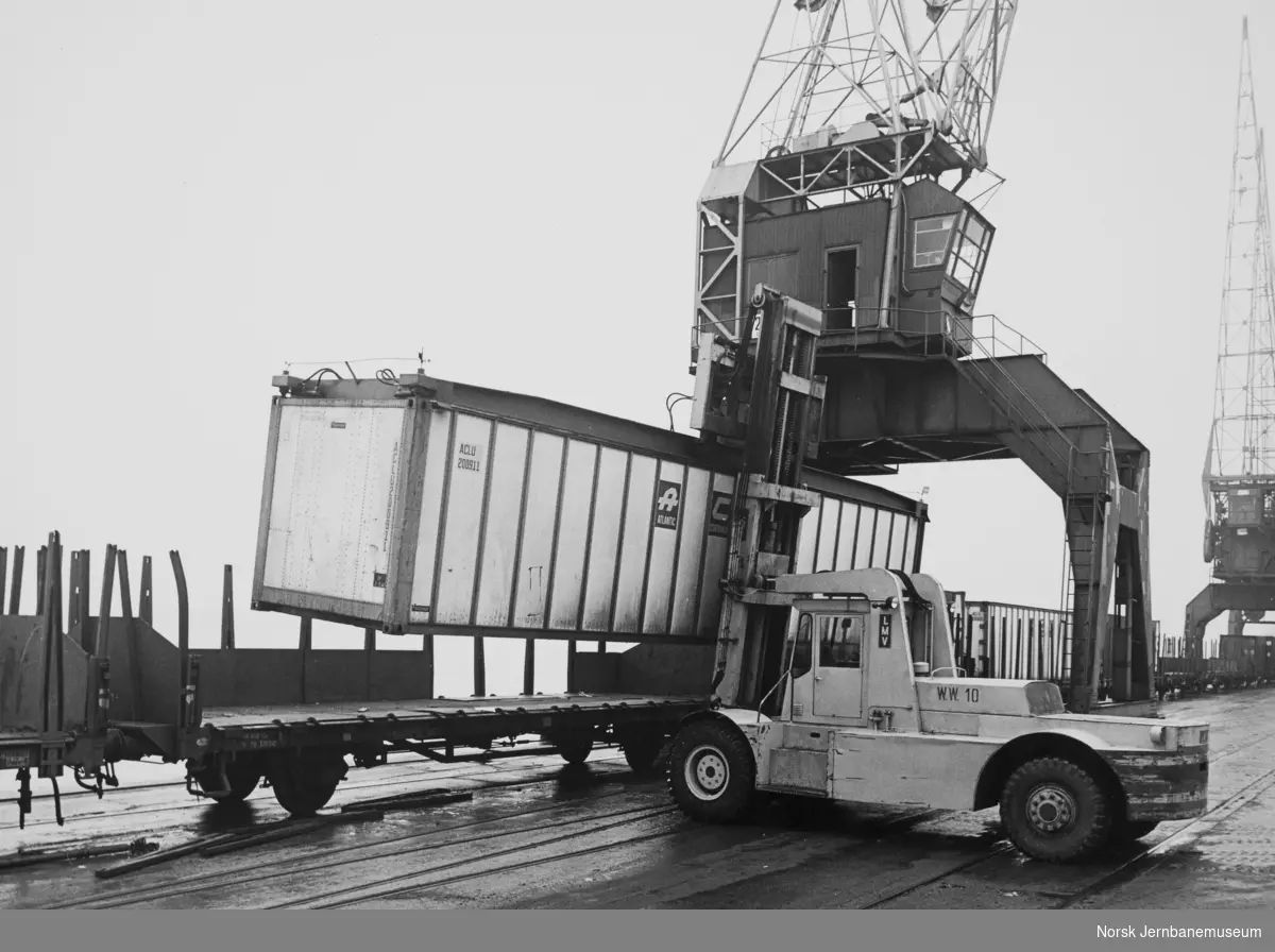 Lasting eller lossing av container med hjullaster - havnekran i bakgrunnen