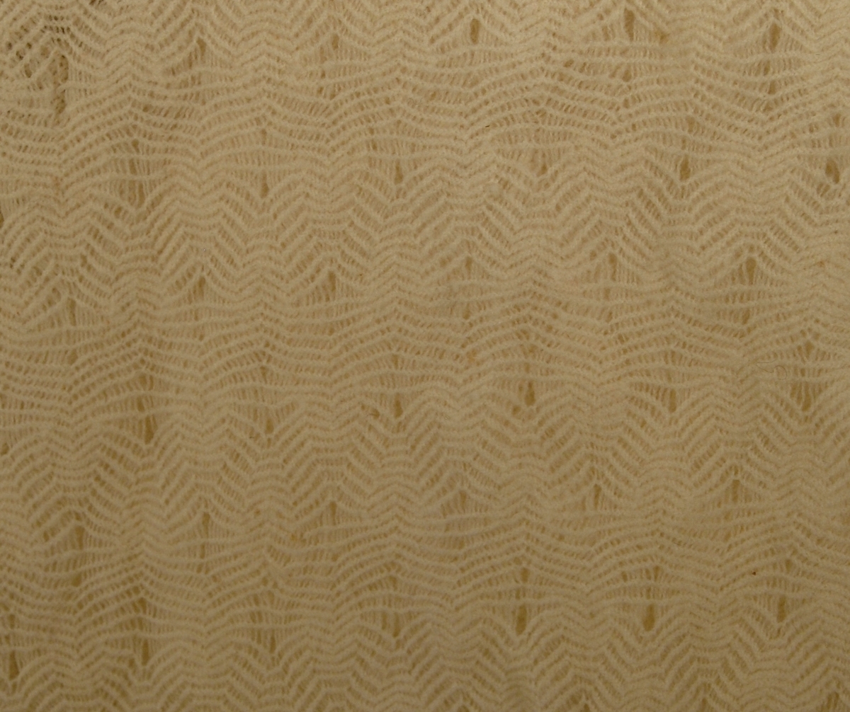 Strikket i tynn ulltråd. Den innerste firkanten er strikket i eit stykke. Knaten rundt påsydd slik at hjørnsne blir avrunda. Dersetter er det påsydd frynser med symaskin.