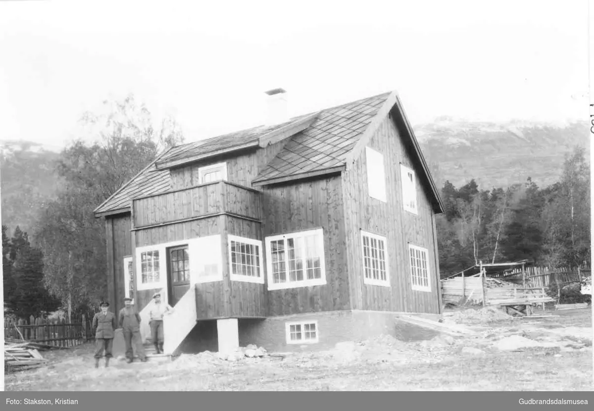 Ole R. Dalen (f. 1897) ved huset sitt opp for Vollungsbrua.  
Vidare mot høgre står Rasmus Holø (f. 1887) og Simen Kolden (f. 1904)