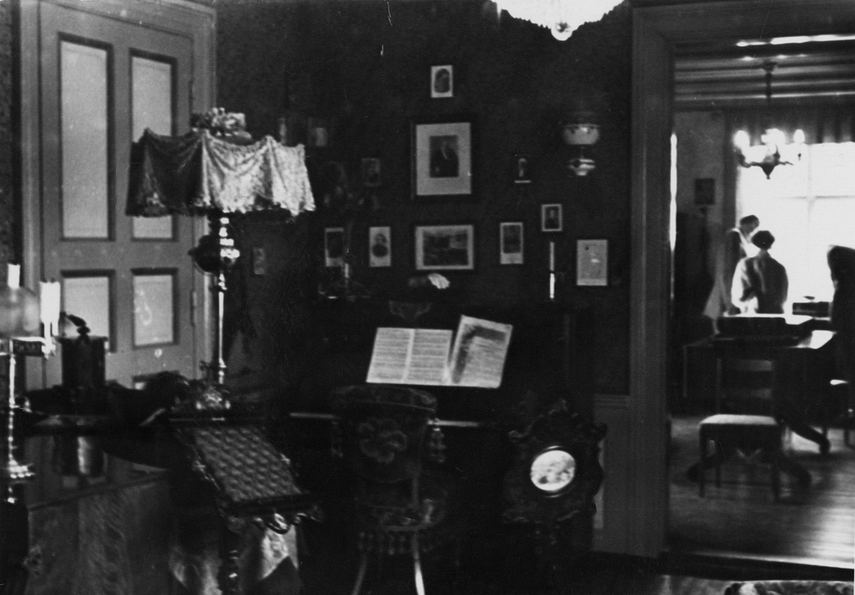 Interiørbilde av Grieg/Tsjajkovskij-rommet, tatt mot hjørnet med Tsjajkovskij-portretter.
Det er en åpen dør inn til det nåværende Patti/Wiborg-rommet hvor det står to personer.