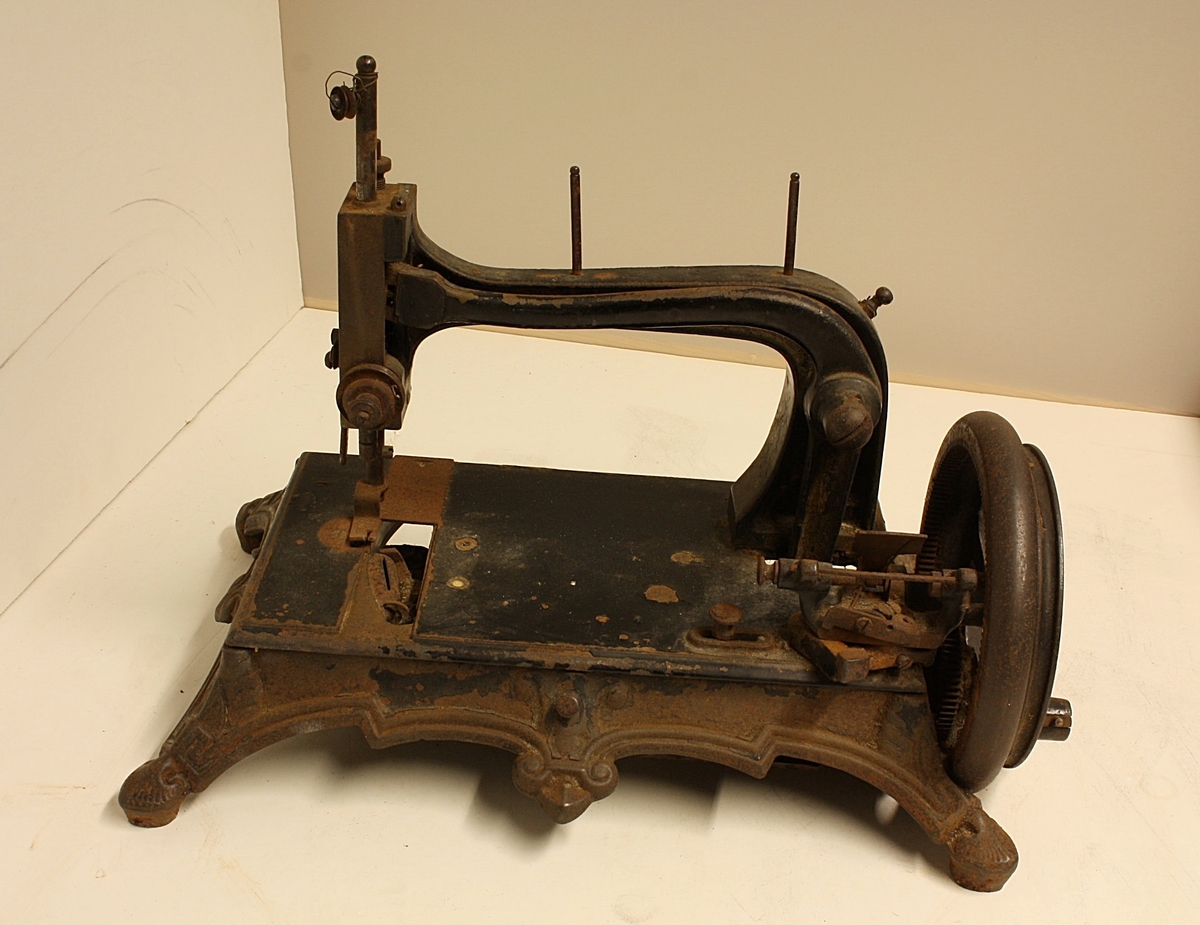 Symaskin. Opererast manuellt med sveiv. 
Tidleg modell som er liten i storleik.