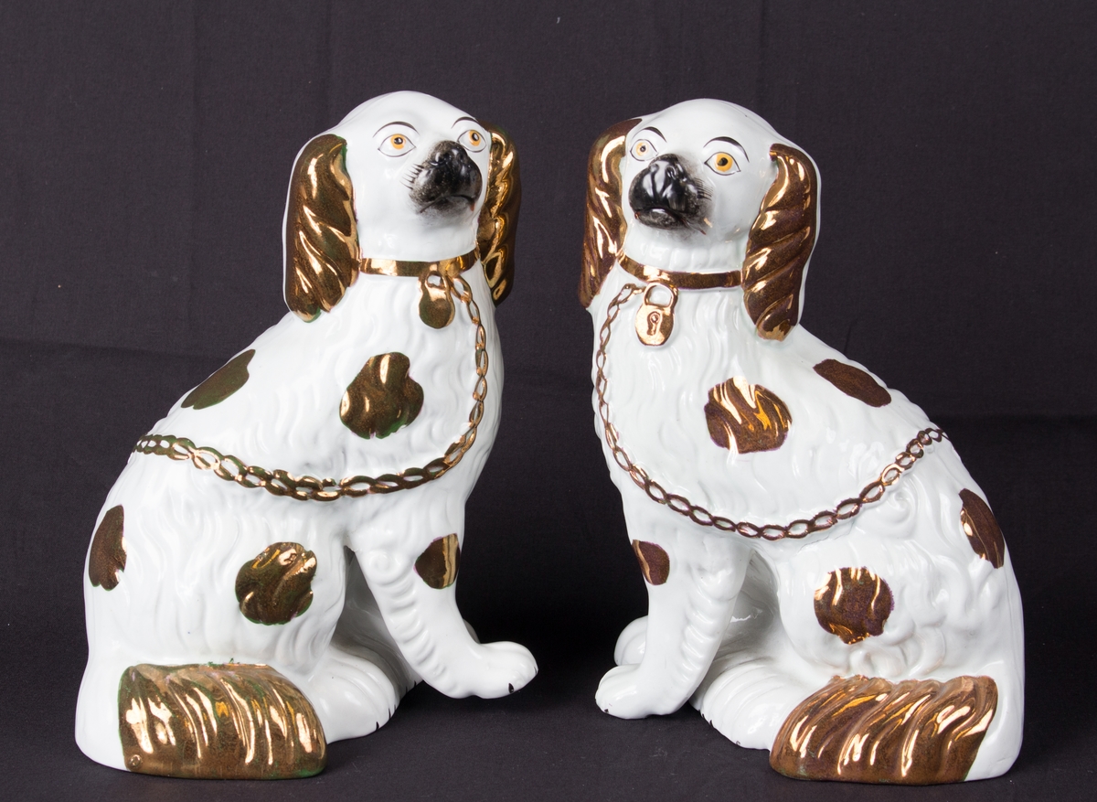 Porselensfigurer som forestiller to hunder som sitter, høyre og venstre, hvit med gulldekor og sorte snuter.
