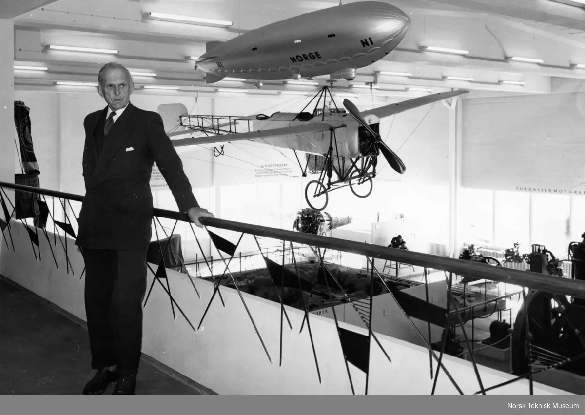 Tryggve Gran besøker flyutstillingen på Norsk Teknisk Museum på Helsfyr. Han står på galleriet, i bakgrunnen hans eget fly "Nordsjøen" og en modell av Roald Amundsens luftskip "Norge". 20.4.1961.