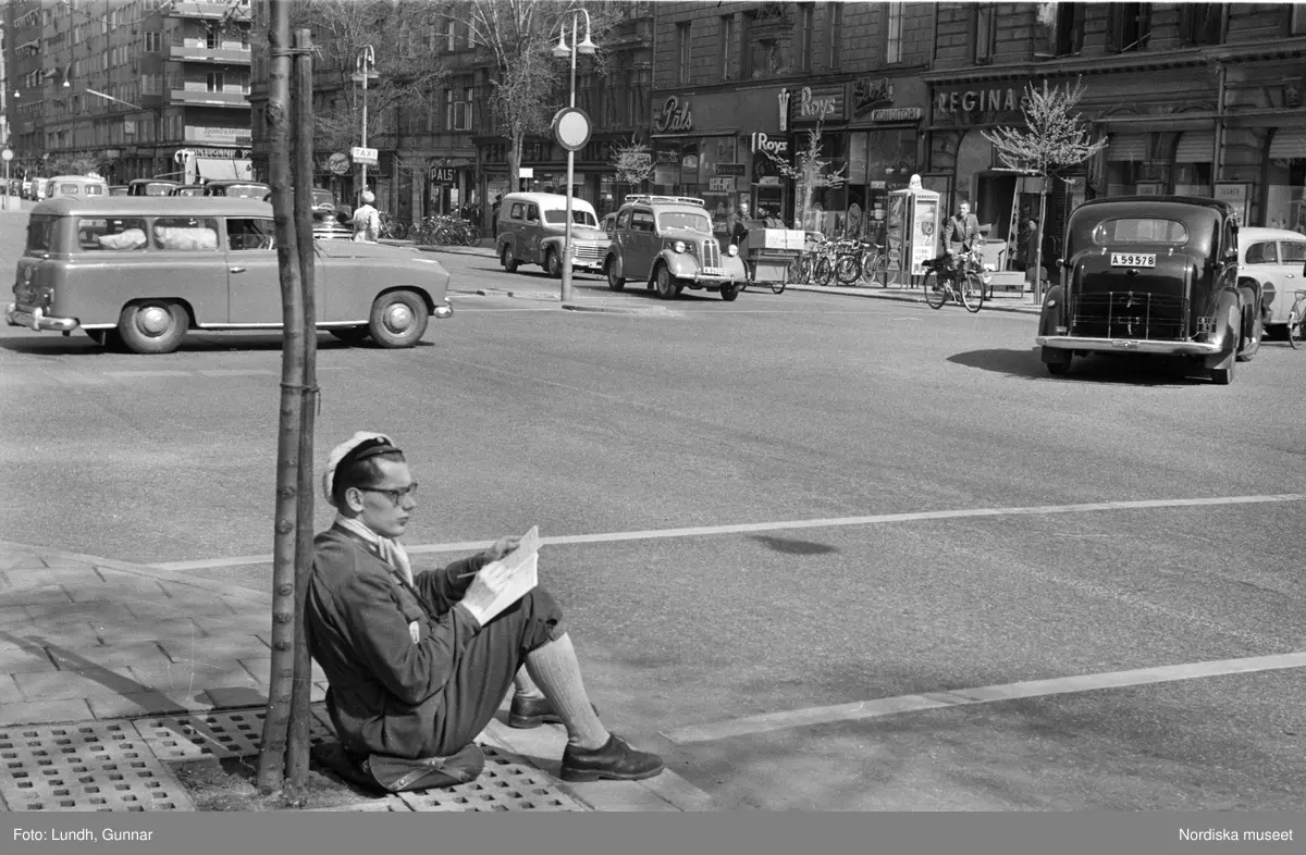 Student sitter med skissblock under träd i gathörn, Stockholm.
