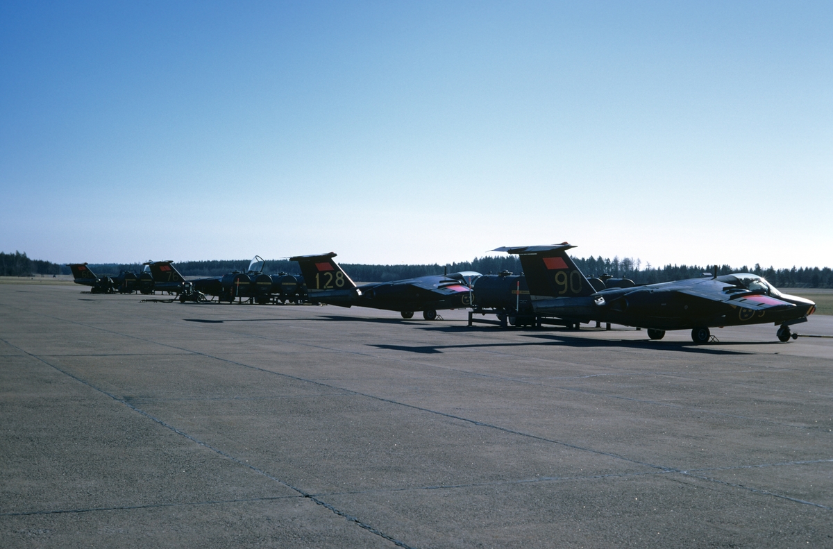 Fyra flygplan SK 60 ur F 5 Krigsflygskolan står på flygfältet på Malmen, 1973. Vy snett bakifrån.
Flygplanen är märkta med nummer 60, 76, 128 samt 90.