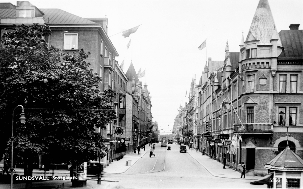 Från vänster kv Bacchus 3B, Storgatan och till höger kv Mercurius. På Storgatan, spårvagn, bilar och fotgängare. Text till bild "SUNDSVALL. Storgatan."