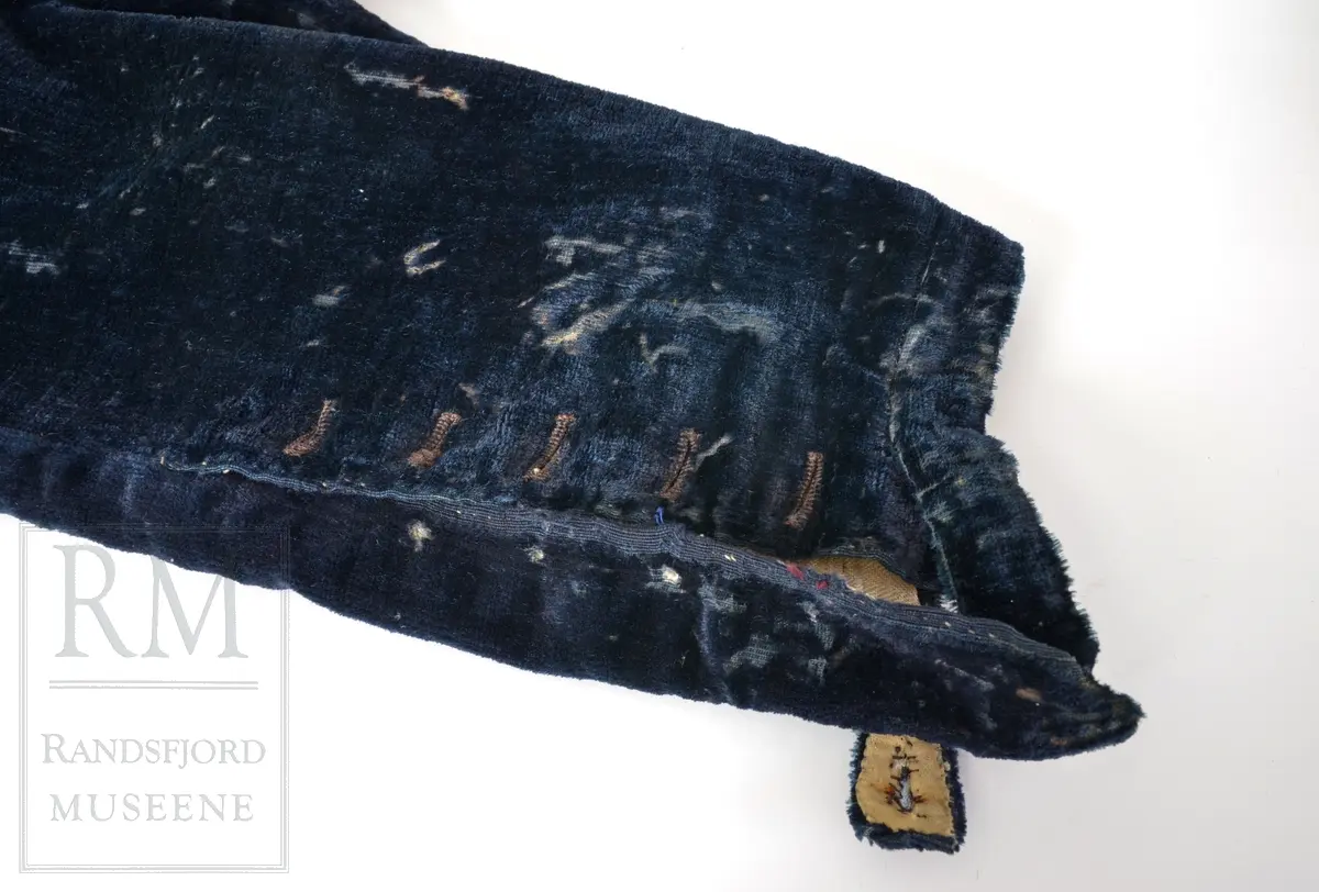 Mørk blå fløyelsbukse, knelang, med lem. Foret i lin. Fem flate messingknapper.