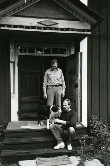 Hemma på Hildings förstukvist i Sunnanåker, Glösbo, 3 juni 1984. Hilding står på trappan och en man sitter på ett av trappstegen och klappar en hund som står bredvid.