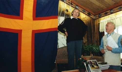 Fotografiet är taget i samband med utgivningen av boken "Förstukvistar i Hälsingland", 1995. Hilding står på en träsoffa och talar. Bredvid hänger en stor flagga. På ett bord framför honom står boken om förstukvistar.
