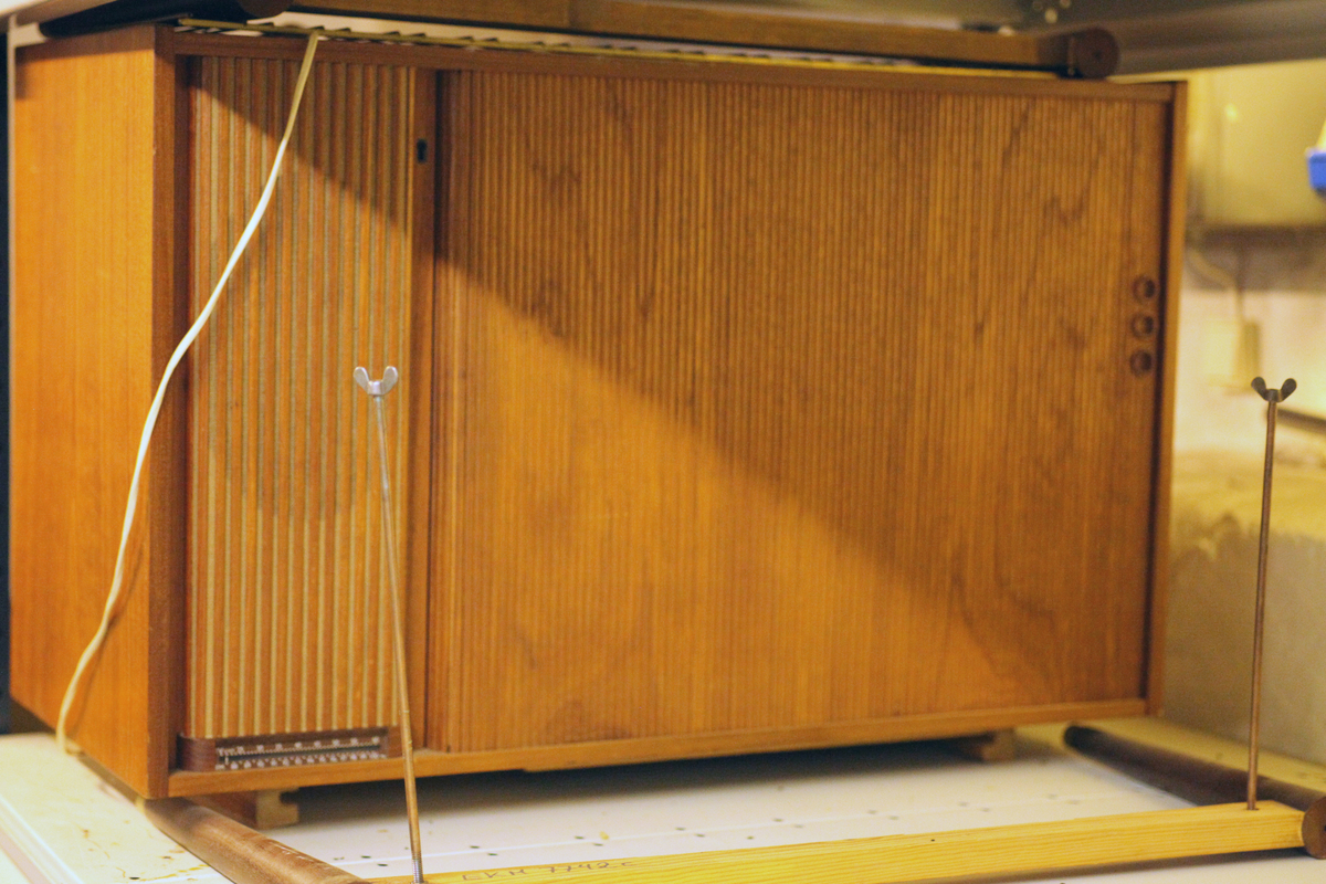 Radionette i teak-kasse med sjalusidør og understell med metallhylle. Kassa skal være produsert på Gjøvik.