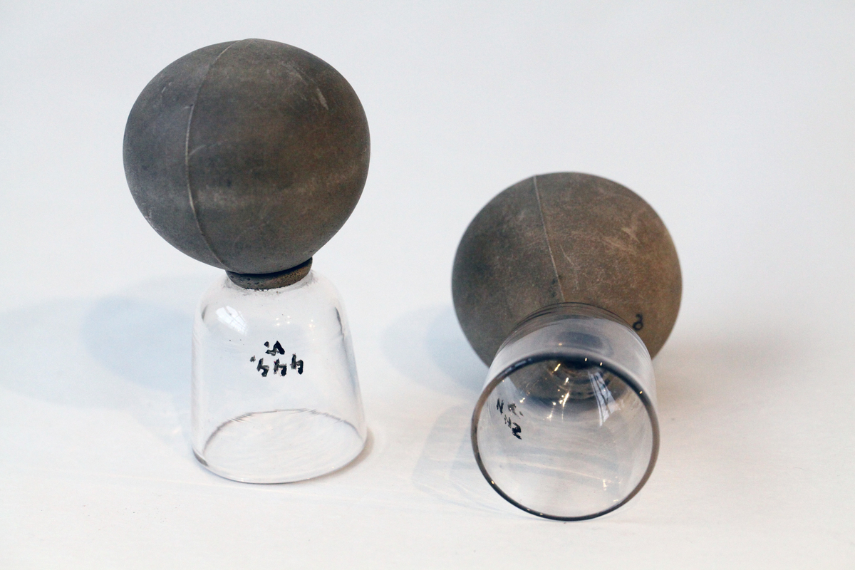 Glassene (b) og (c) har en knopp på toppen, og glass (a) har ei kule av grå gummi på toppen.