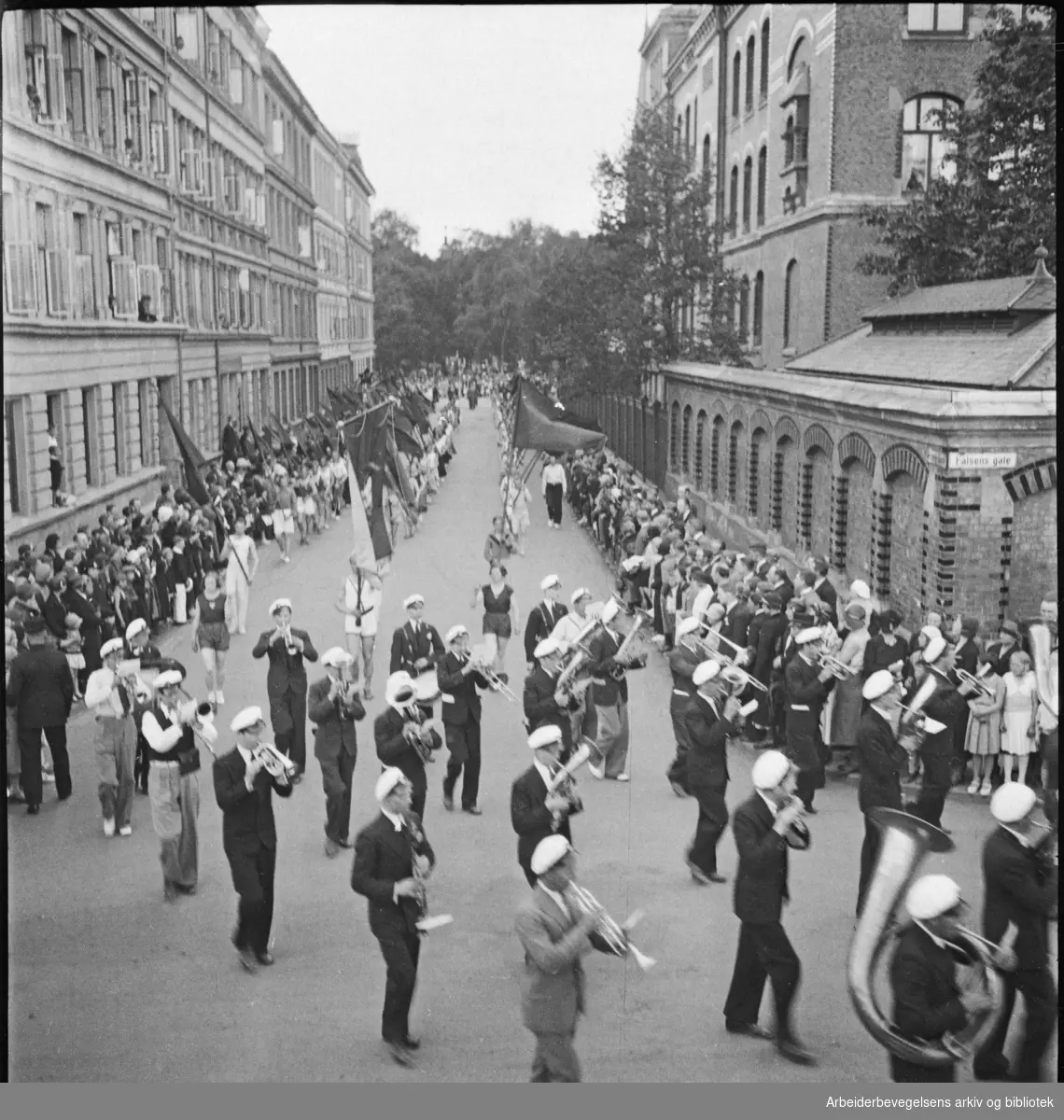 1. Mai-toget 1932 på vei til Dælenenga idrettsplass. Musikkorps. Bildet er tatt på hjørnet av Falsens gate og Nissens gate, med Birkelunden i bakgrunnen. Grünerløkka skole til høyre.