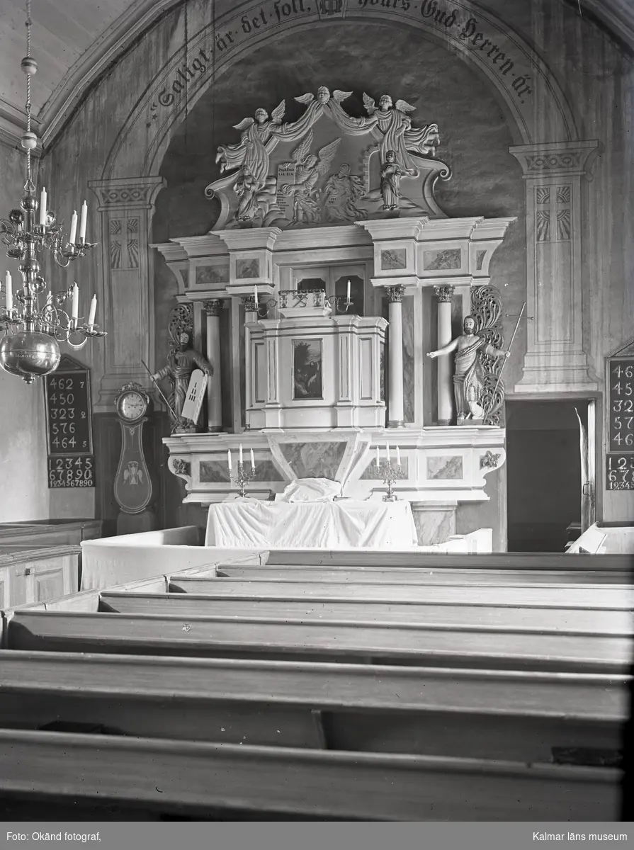 Interiör av Ås kyrka. Psalmtavla, moraklocka, altare, kyrkbänkar och predikstol ovanför altaret.