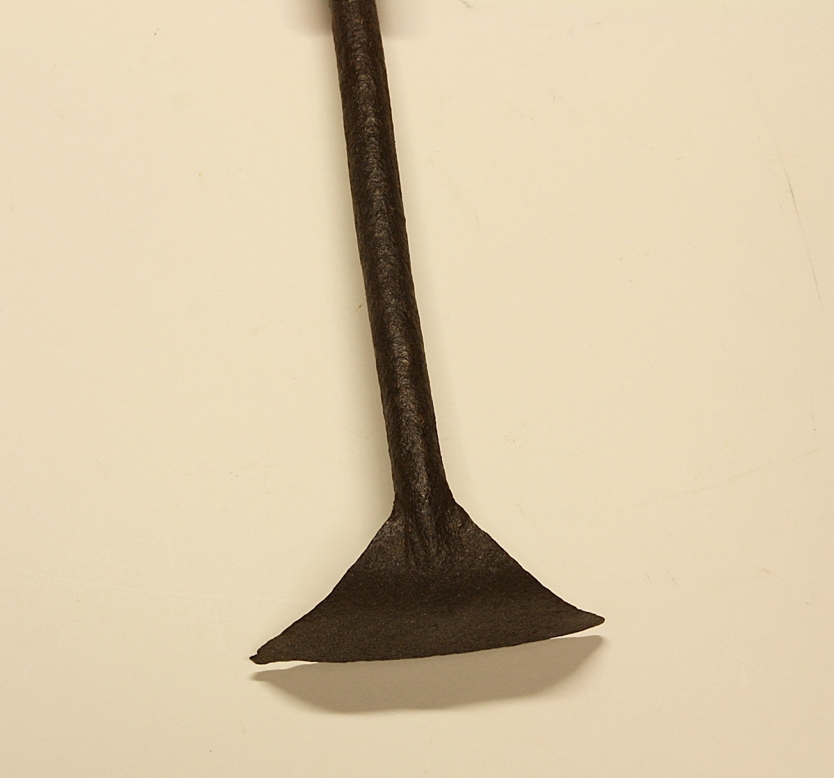 Grovt tilvirket treskaft. Langt metallskaft festet med to store spiker/nagler til treskaftet. Vifteformet, trekantet blad.