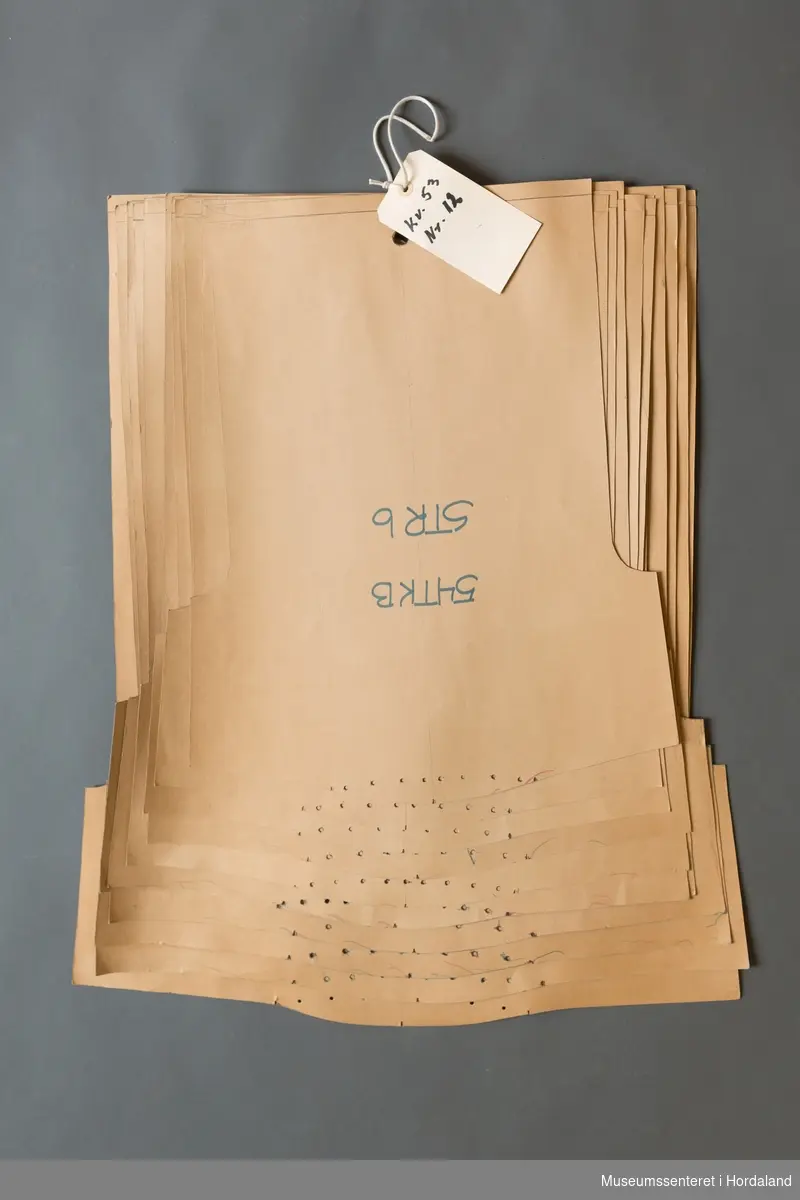 Mønsterskantar i papp, brukt til å skjere ut ulike delar av plagg i klesproduksjon. Desse er til ein t-skjorte i kvalitet 53, nr. 14, str. 14-60.