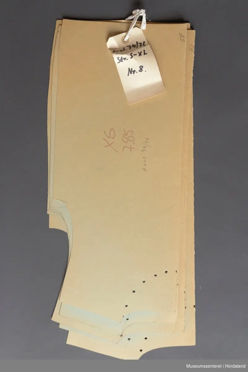 Mønsterskantar i papp, brukt til å skjere ut ulike delar av plagg i klesproduksjon. Desse er til overdelar i kvalitet 74/76, str. S-XL, nr. 8.